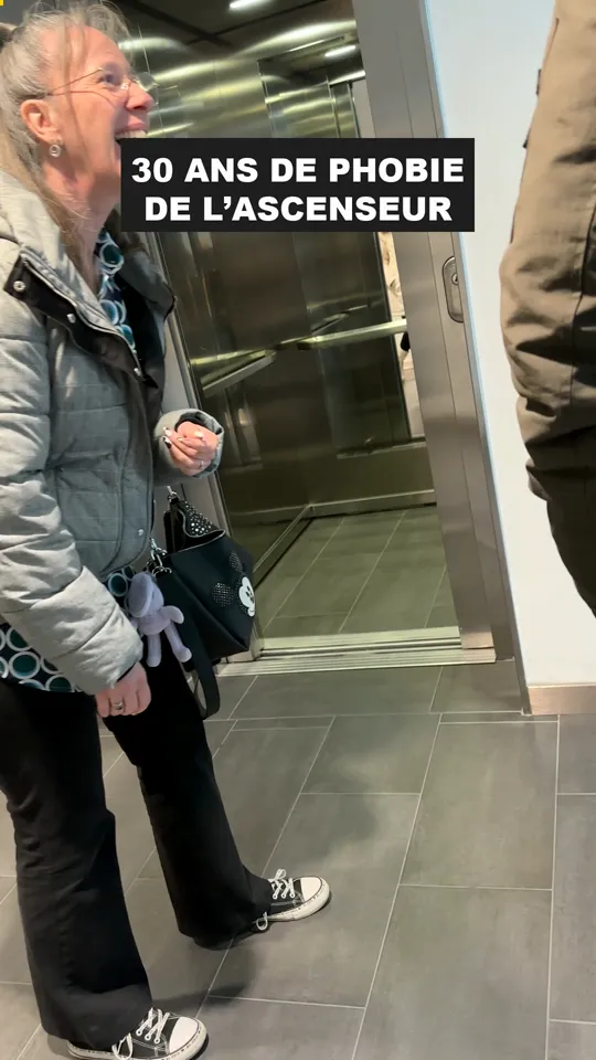 Alexandra rit devant la porte ouverte d'un ascenseur